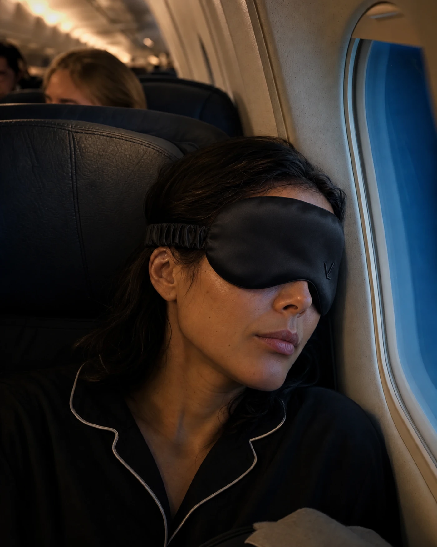 Una mujer durmiendo en el asiento de ventanilla de un vuelo nocturno, con VEIL puesto